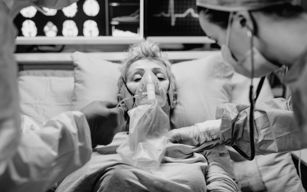 Woman wearing oxygen mask receiving medical assistance from doctors.