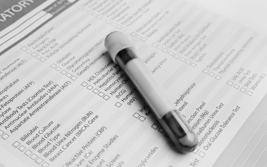 A lab test tube containing a blood sample, alongside a list of various blood work tests.