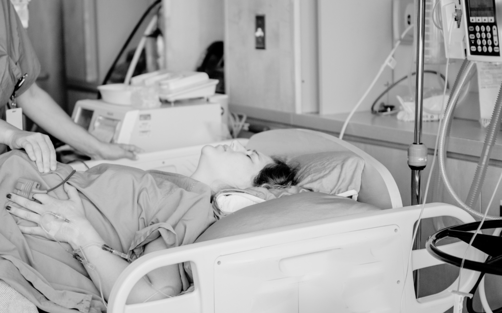 A woman in a hospital bed, clutching her stomach in pain during childbirth.
