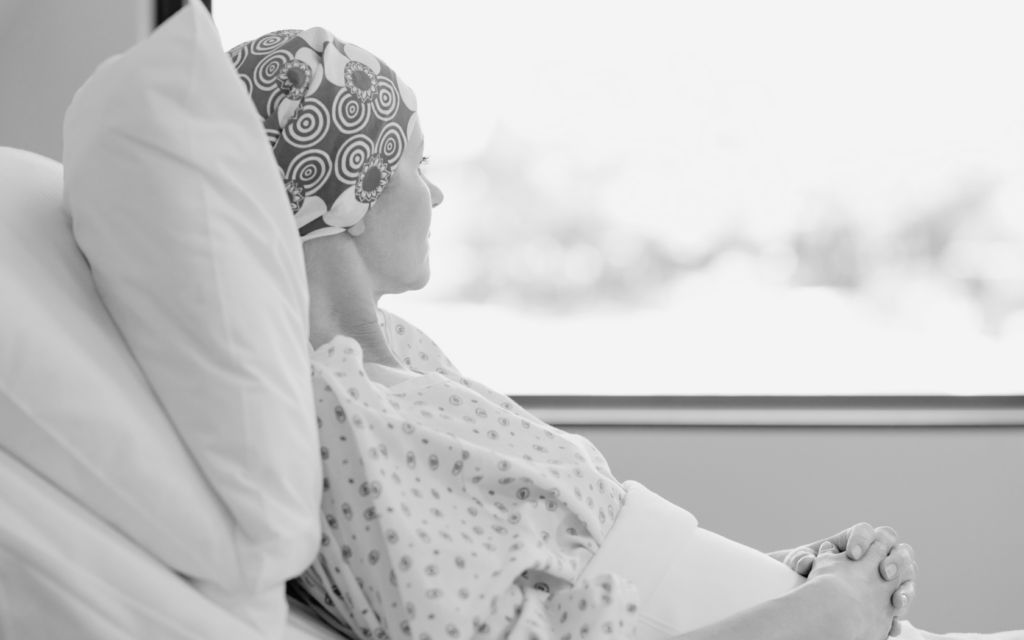 A woman with cancer lying in a hospital bed, gazing out the window.