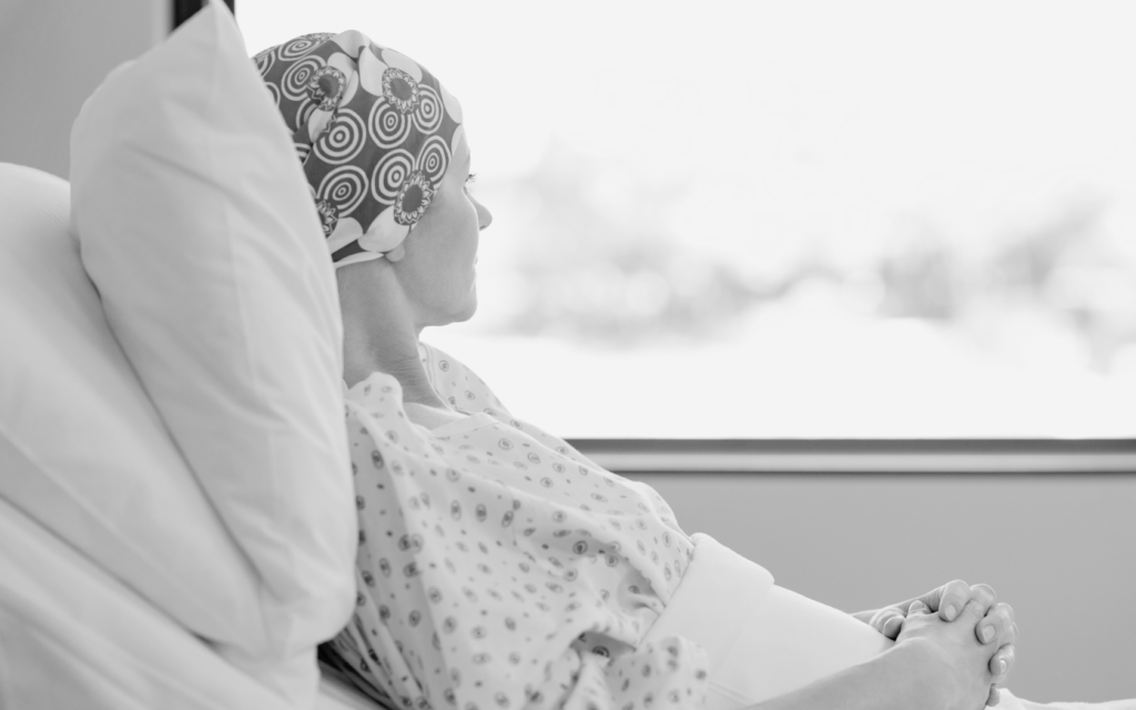 A woman with cancer lying in a hospital bed, gazing out the window.