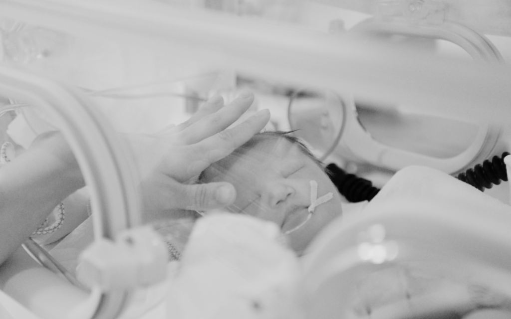 Mother gently touching her baby through an incubator in the NICU.