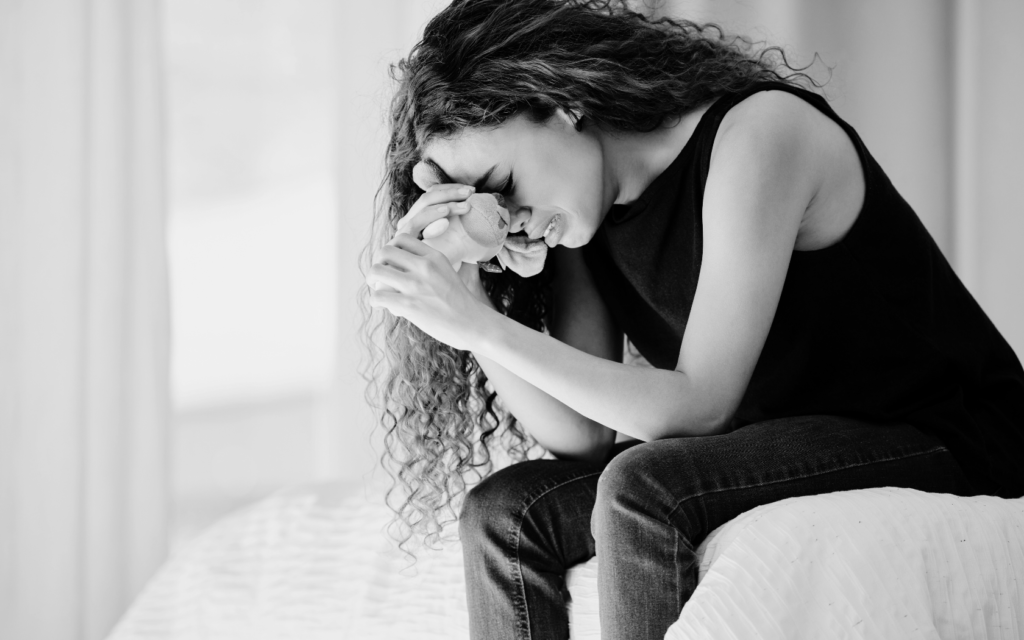 Woman holding a stuffed toy, sitting on the edge of a bed grieving