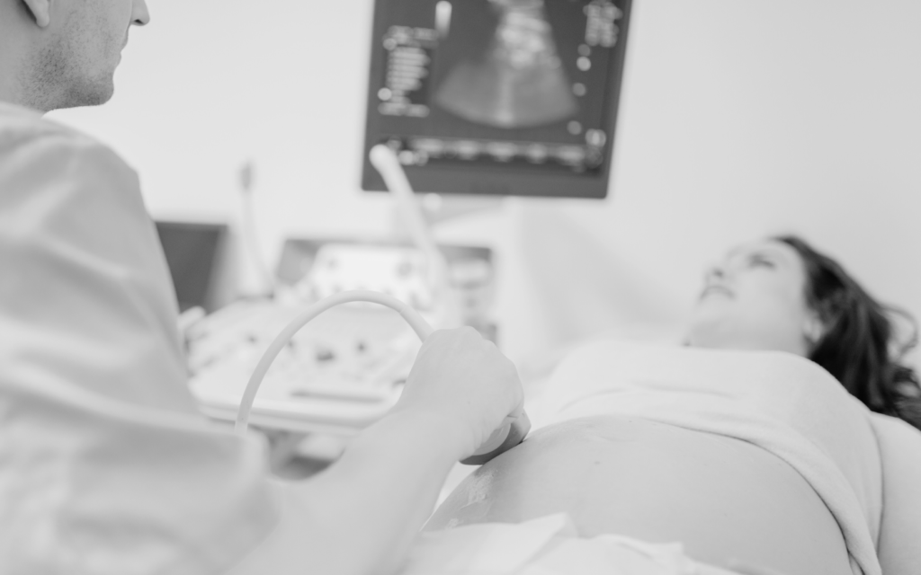 Doctor performing an ultrasound on a pregnant woman, with the baby’s image on the monitor.